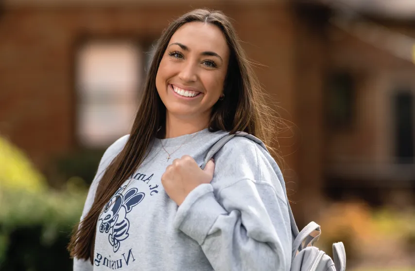 Student with backpack standing outdoors, smiling.