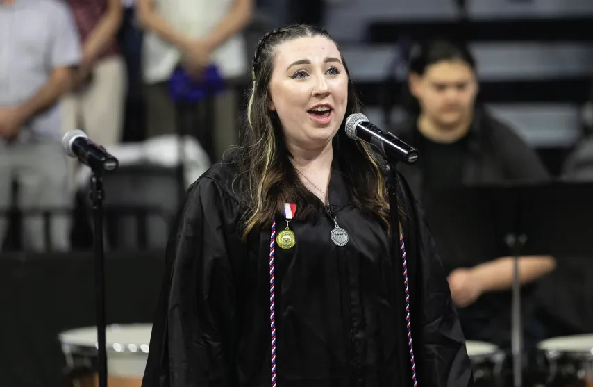 Student in graduation gown singing at commencement event.